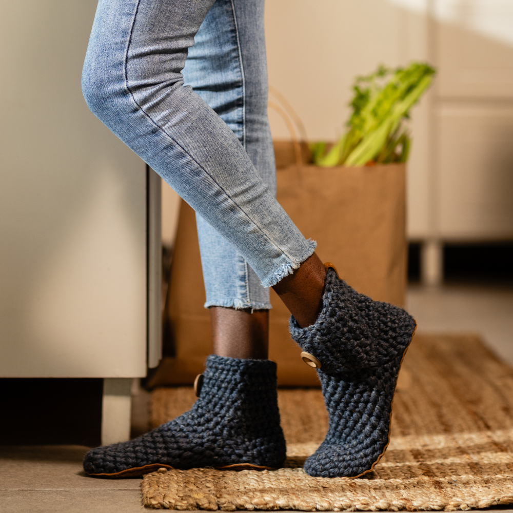 Person wearing dark grey knitted slippers with jeans in a home setting
