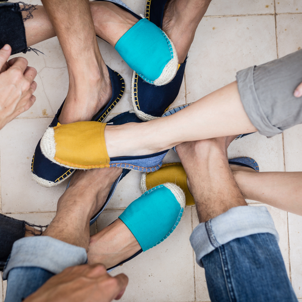 Four pairs of feet wearing colorful espadrilles on a tiled floor.