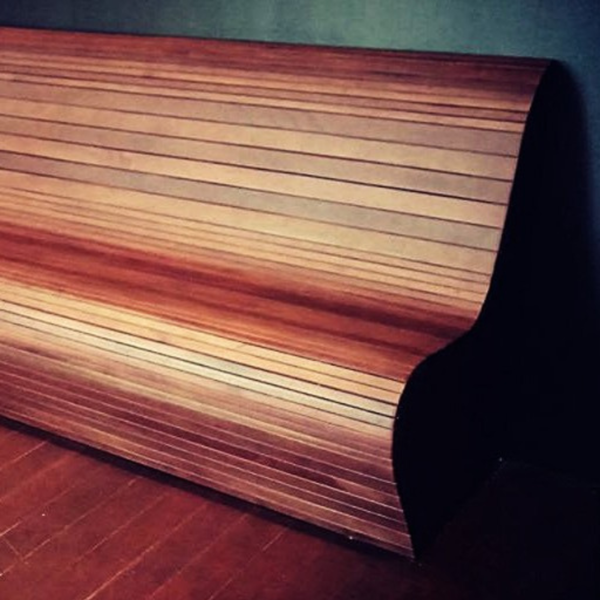 Wooden seat with a wavy design against a dark wall.