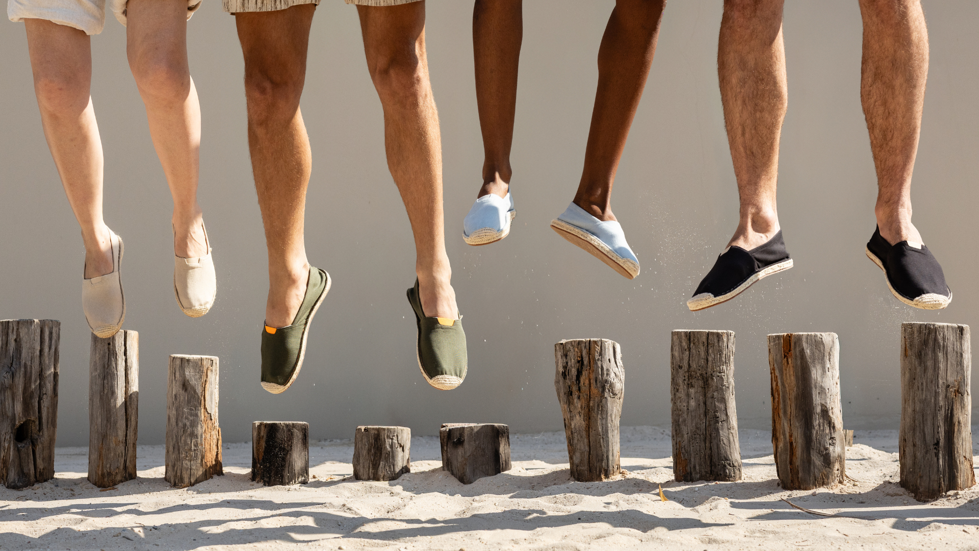 People jumping over wooden logs on a sandy surface wearing cotton espadrilles