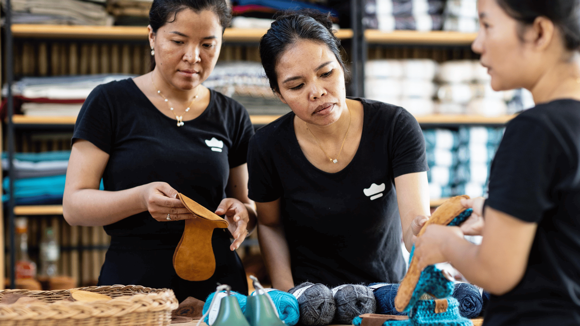 Three women in black shirts working with yarn and knitting tools in a workshop setting.