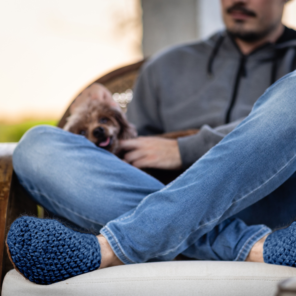 Person sitting on a couch with a dog in their lap, wearing light blue slippers.
