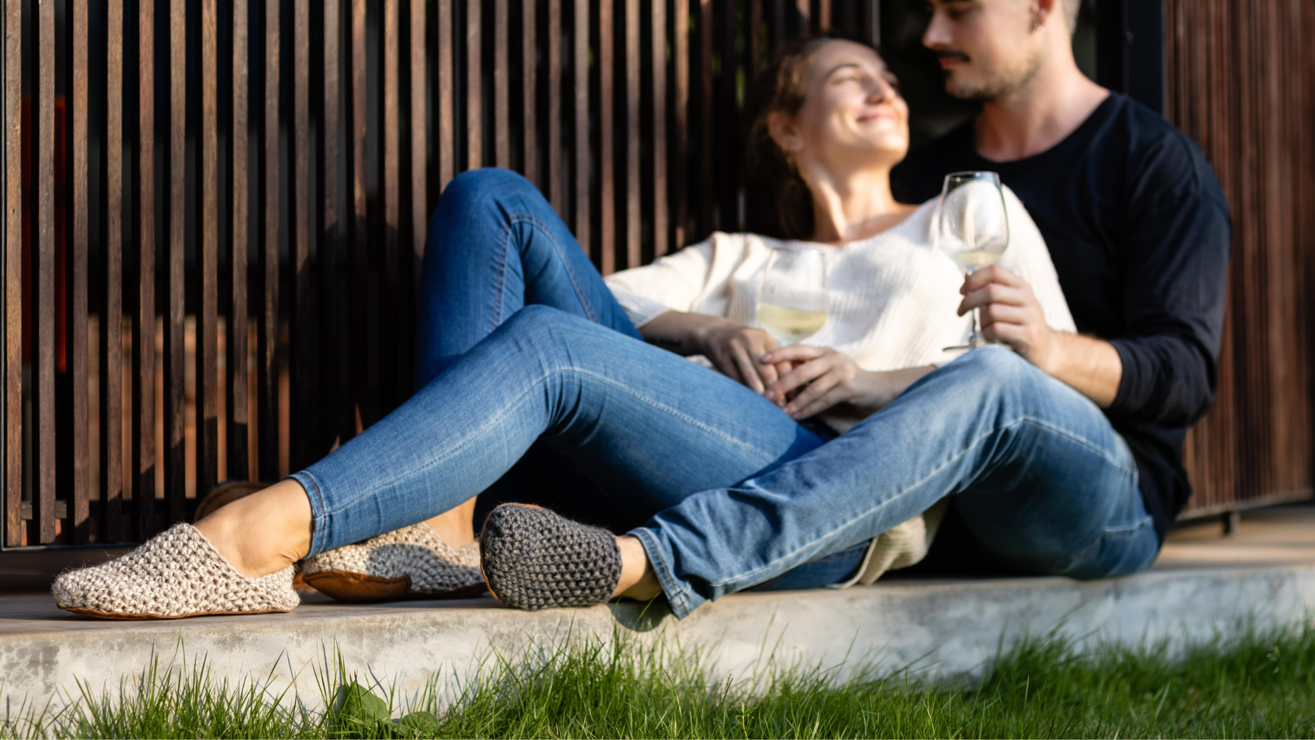 Two people sitting together outdoors, one holding a glass of wine. Wearing light wool slippers